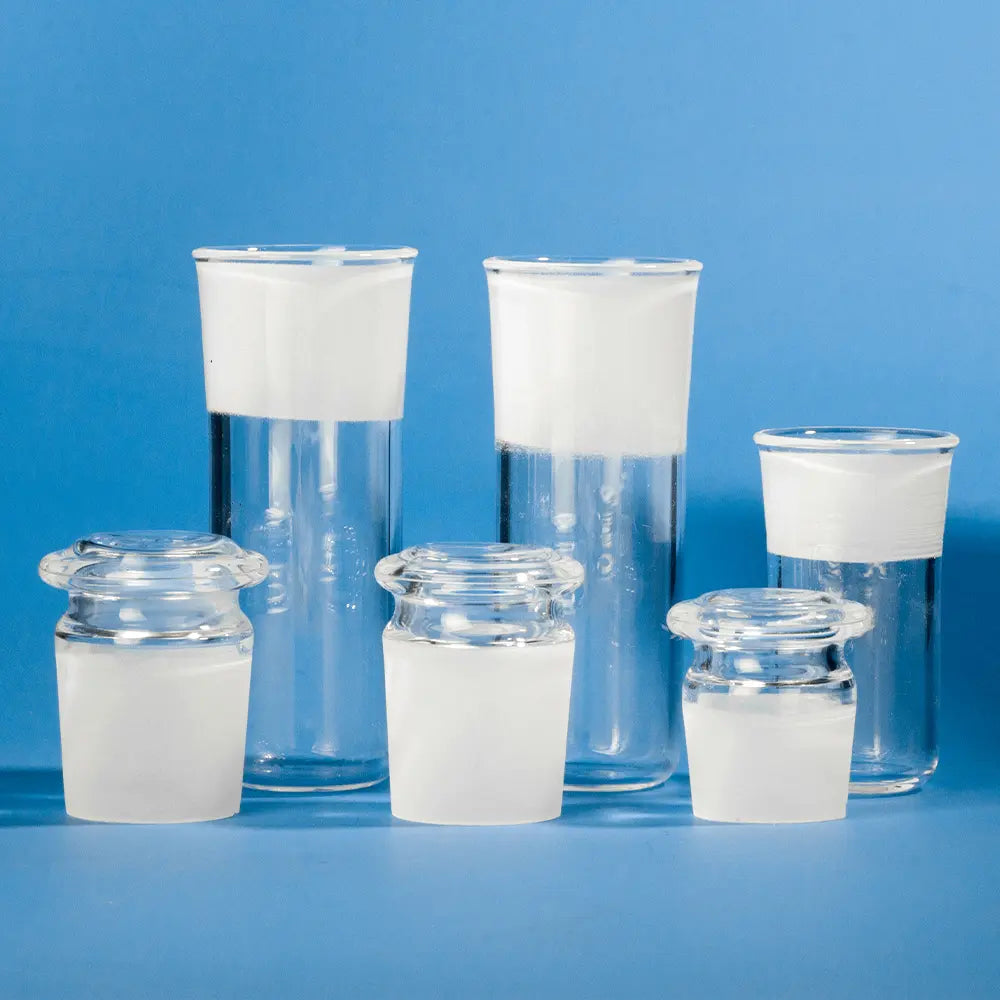 A close-up view of three clear quartz test tubes with frosted plugs, standing upright in a row on a blue surface