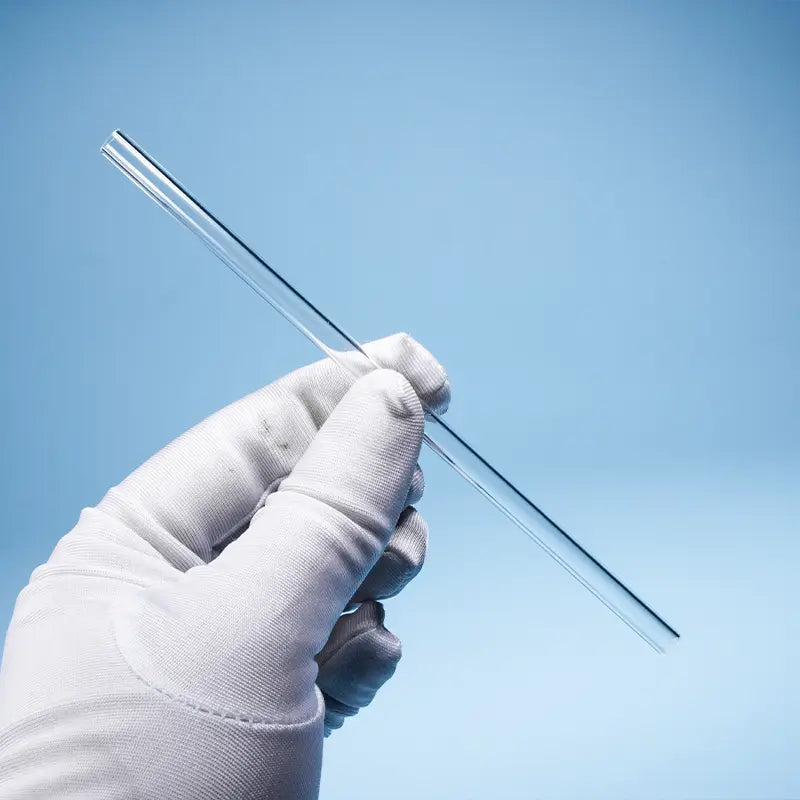 A gloved hand holding a single, perfectly clear high-precision quartz capillary tube.